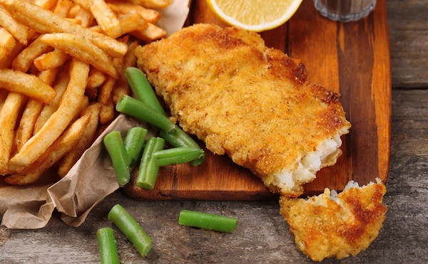 Breaded fried fish fillet and potatoes with asparagus and lemon on cutting board and rustic wooden background