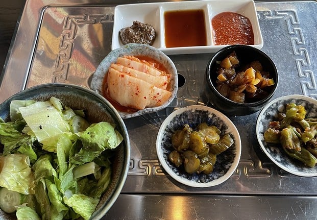 A bowl of sesame-scented salad joins traditional banchan snacks at the center of the table at Nami Korean Steakhouse: Spicy kimchi, three variations on cooling, tangy greens. and three hot sauces.