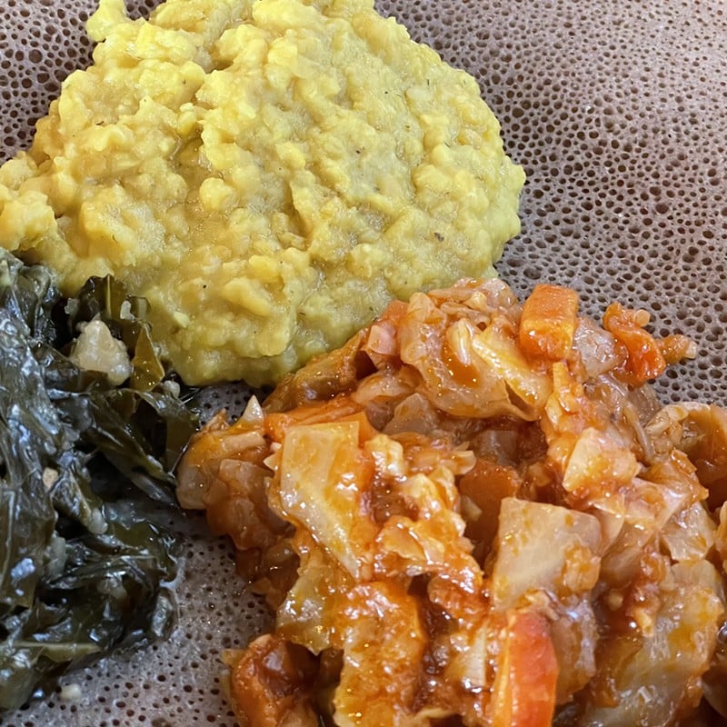 A closer look at misir wot (yellow lentil stew), red-sauced and spicy cabbage atakilt and gomen wot collard stew on a veggie combination.